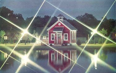 A small red school house across a pond.